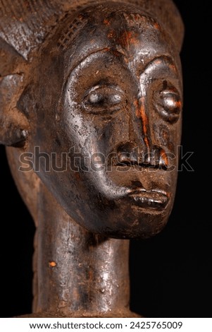 Close-up of an African female figure carved in wood isolated on black. Traditional African art with balanced shapes and volumes and a beautiful dark brown patina.