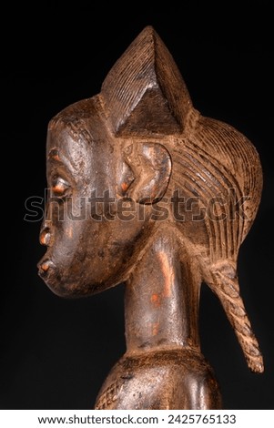 Close-up of an African female figure carved in wood isolated on black. Traditional African art with balanced shapes and volumes and a beautiful dark brown patina.