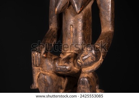 Close-up of an African female maternity figure with baby carved in wood isolated on black. Traditional African art with balanced shapes and volumes and a beautiful dark brown patina.
