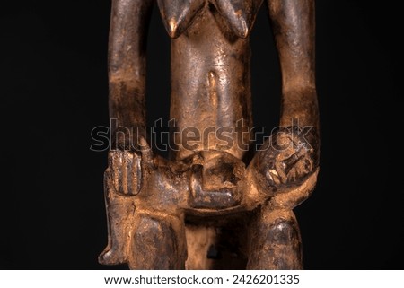 Close-up of an African female maternity figure with baby carved in wood isolated on black. Traditional African art with balanced shapes and volumes and a beautiful dark brown patina.