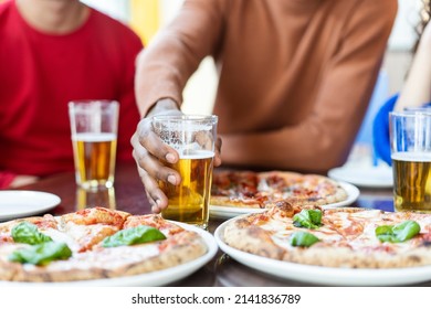 Close-up of african guy's hand taking glass of beer at pizza restaurant - Multi ethnic Friends having fun eating pizza and drinking beer at pub - Powered by Shutterstock