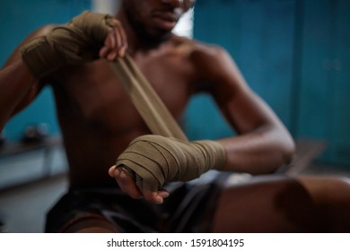 Close-up of African shirtless boxer sitting and wrapping bandage on his hands he is going to sports training - Powered by Shutterstock