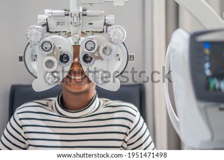 Close-up Of african teen girl Doing Eye Test On Phoropter, African teen girl checking on her eye with optometry machine.