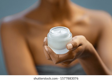 Closeup of african woman holding moisturizer cream jar. Detail of black hands holding face lotion. Woman showing white moisturiser for healthy skin.