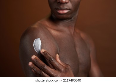 Close-up Of African Young Man Applying Cream On His Body For Protection Isolated On Brown Background