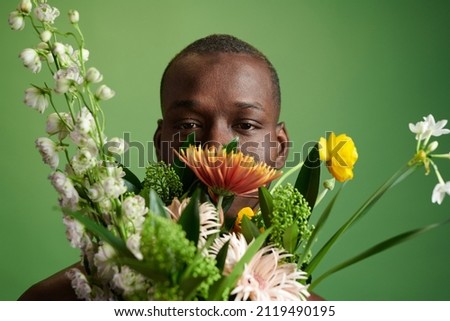 Close-up of African young man hiding behind the beautiful summer bouquet isolated on green background