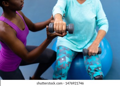 Close-up of African-american female trainer assisting disabled Caucasian senior woman to exercise with dumbbell in sports center. Sports Rehab Centre with physiotherapists and patients working - Powered by Shutterstock