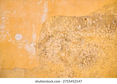 Close-up of an aged building facade featuring cracked yellow paint and exposed sandstone. Minimalist background with organic decay and erosion.
