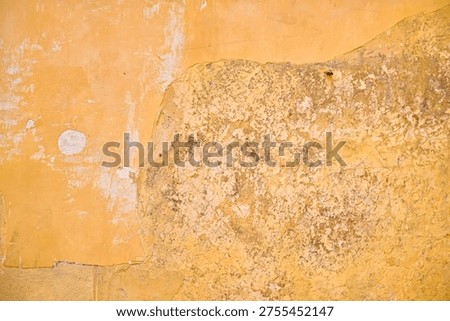 Close-up of an aged building facade featuring cracked yellow paint and exposed sandstone. Minimalist background with organic decay and erosion.