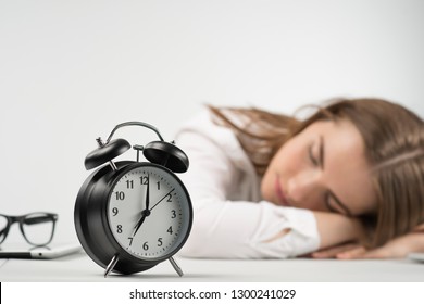 Closeup alarm clock in focus against blurring background with  girl puts her head on the table