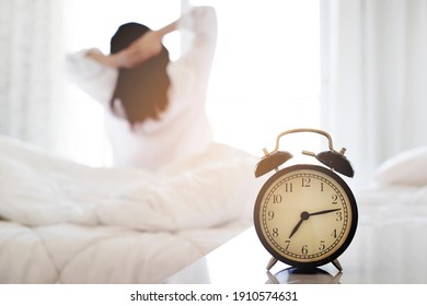 Closeup Alarm Clock Having A Good Day With Background Happy Woman Stretching In Bed After Waking Up, Sunlight In Morning.