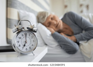 Closeup of alarm clock with senior woman in deep sleep at home. Old woman sleeping in bed next to alarm clock in morning. Elderly woman sleeping in bedroom peacefully. - Powered by Shutterstock