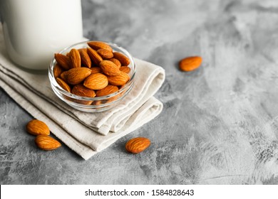 Close-up of almonds in a glass plate, next to a glass bottle with almond milk on a concrete table.