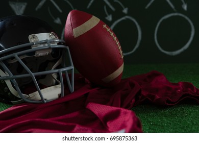 Close-up of American football jersey, head gear and football lying on artificial turf against strategy board - Powered by Shutterstock