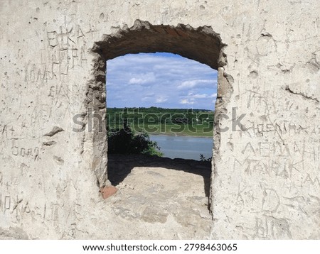 Close-up of an ancient stone window frame at Khotyn Fortress, Ukraine, featuring historic graffiti and inscriptions on the walls, overlooking the Dniester River