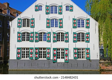 Closeup of ancient waterfront house facade, many glass windows, open exterior board batten shutters painted in triangle red white design - Lier, Belgium 