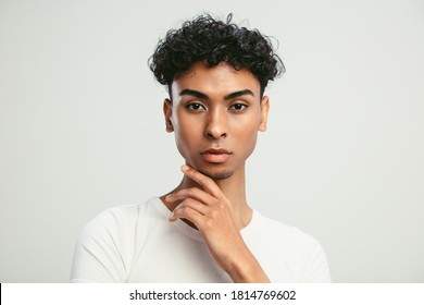 Close-up of an androgynous man with his hand on chin. Young guy with feminine facial features looking at camera against white background.