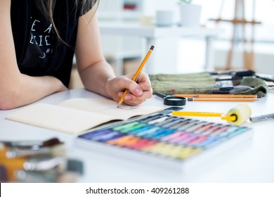 Close-up angle view of a female painter drawing draft at sketchbook using pencil. Artist sketching in art studio with crayons set. - Powered by Shutterstock