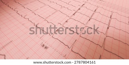 Close-up angled view of a printed electrocardiogram (ECG) graph showing heartbeat tracings on pink grid paper with a shallow depth of field.