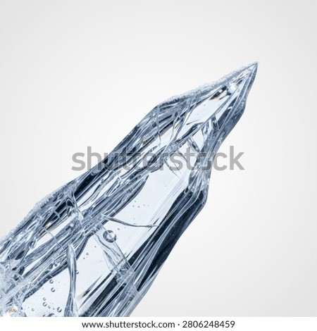 A close-up, angled view of a sharp, elongated, transparent ice crystal fragment with angular facets and internal air bubbles, isolated on a light gray