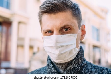 Close-up of an angry or surprised young man in a medical mask standing on the street and looking at the camera. Portrait of a guy who raised one eyebrow in surprise
