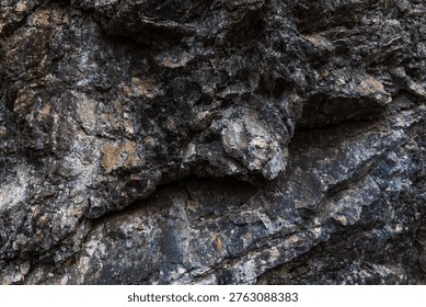 A close-up of an angular rock formation featuring sharply defined layers and fractured geological structures. The rugged stone surfaces display mineral textures and natural weathering, highlighting the complex patterns formed by geological forces over time.