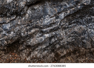 A close-up of an angular rock formation featuring sharply defined layers and fractured geological structures. The rugged stone surfaces display mineral textures and natural weathering, highlighting the complex patterns formed by geological forces over time.