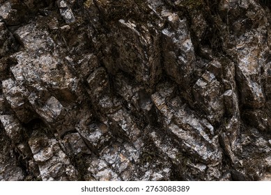 A close-up of an angular rock formation featuring sharply defined layers and fractured geological structures. The rugged stone surfaces display mineral textures and natural weathering, highlighting the complex patterns formed by geological forces over time.