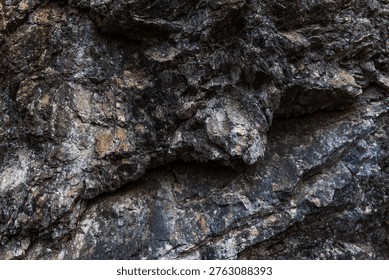 A close-up of an angular rock formation featuring sharply defined layers and fractured geological structures. The rugged stone surfaces display mineral textures and natural weathering, highlighting the complex patterns formed by geological forces over time.