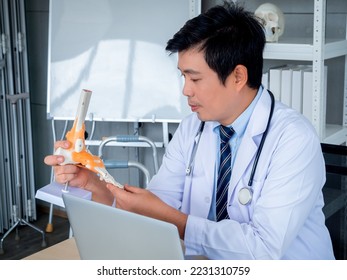 Close-up ankle joint foot skeleton anatomy model holding by orthopedic Asian doctor male with laptop computer, video conference with patient in medical office. Telemedicine with physician concept. - Powered by Shutterstock