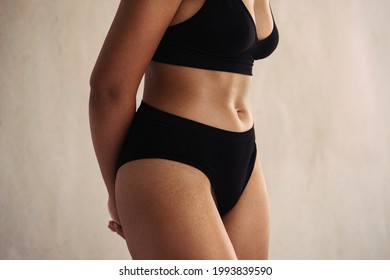 Closeup of an anonymous natural female body wearing black underwear. Young body positive woman embracing her natural body while standing alone against a studio background.