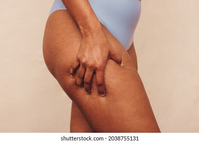Closeup of an anonymous woman grabbing her thigh in a studio. Unrecognizable woman standing in blue underwear against a studio background. Body positive woman embracing her natural body.