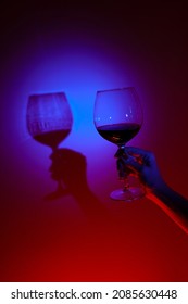 Closeup Of Anonymous Woman Hand Holding Glass Of Wine Over Fashion Blue Wall, Neon Blue Light On Wall. Colorful Light, Minimalism Concept. 