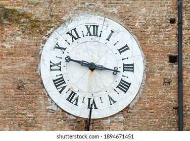 Close-up Of An Antique Big Marble Clock With Roman Numerals On The Brick Wall Of An Old Building, Siena, Tuscany, Italy