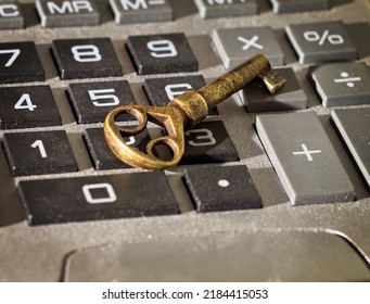 Close-up Of Antique Brass Key Resting On Old Dusty Calculator Keyboard. Key Is Side Lit With Shadows And Highlights