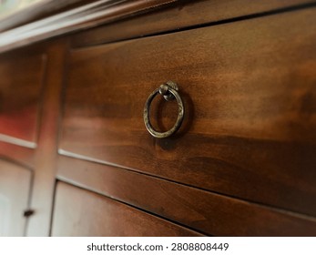 Close-up of an antique brass ring pull handle on a warm cherry wood drawer of a vintage dresser.