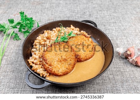 Close-up of appetizing fried fish cutlets made from carp with loose spelt porridge and rich gravy (sauce), served in a traditional cast iron skillet on a textured tablecloth. The dish is garnished wit