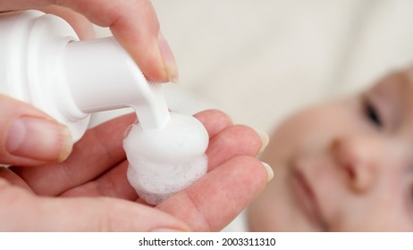 Closeup of applying medication lotion on red baby cheek suffering from dermatitis and acne. Concept of newborn baby hygiene, health and skin care.