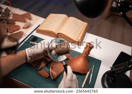 Close-up of an archaeologist working late in the office studying an artifact of an ancient culture using a magnifying glass. Copy space