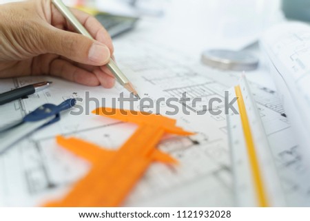 Close-up Architect or engineer hands working on blueprint plans  with  a pencil,  a ruler, calculator, smartphone, laptop and engineering tools. Architect or engineer working on blueprint in office. 
