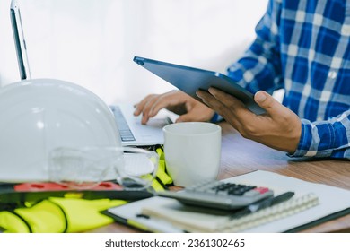 Close-up of an architect or engineer's hand holding a tablet to be creative in project design and drafting in the office and calculate the construction budget estimate on the work desk