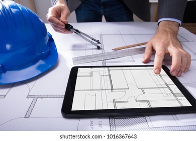 Close-up Of Architect's Hand Using Digital Tablet With Blueprint On Desk