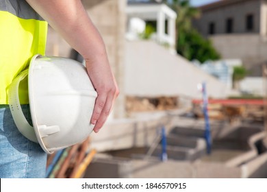 Close-up of an architect's hand wearing a safety vest and holding a white helmet, while standing at the construction site of a private property, supervising, inspecting or overseeing the work progress - Shutterstock ID 1846570915