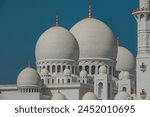 A close-up architectural shot of a majestic mosque featuring white marble domes adorned with golden spires under a clear blue sky.