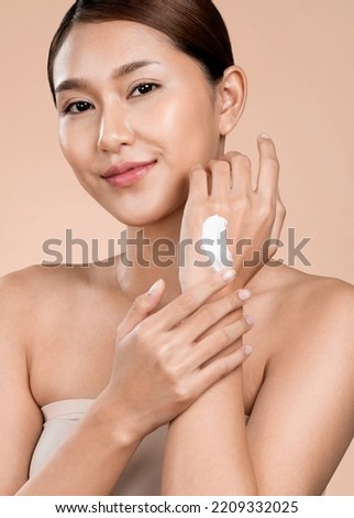 Closeup ardent girl with soft makeup looking at camera, applying moisturizing skincare cream on her hand, isolated background. Skincare cream applied by female model concept.