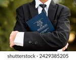Closeup of the arms of a young boy with his arms folded around the Book of Mormon. Boy in suit and tie.