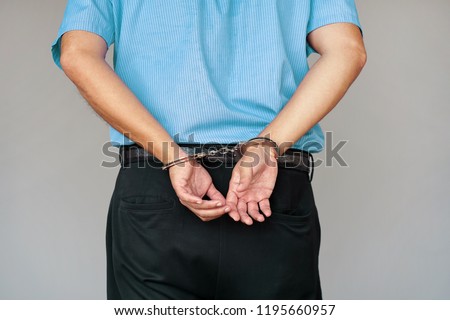 Close-up. Arrested man handcuffed hands at the back. Isolated on gray background. Businessman in office in handcuffs holding a bribe. Arrested man in handcuffs. Criminal hands locked in handcuffs.