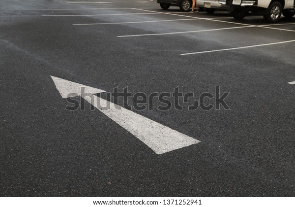 Closeup of arrow on asphalt ground of the parking\
lot after raining. The traffic sign show the symbol of safty and\
right direction to the\
goal.