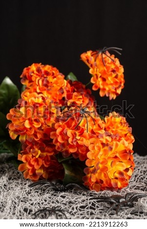 Close-up of artificial orange flowers with plastic spiders on table with Hallween decoration, vertical