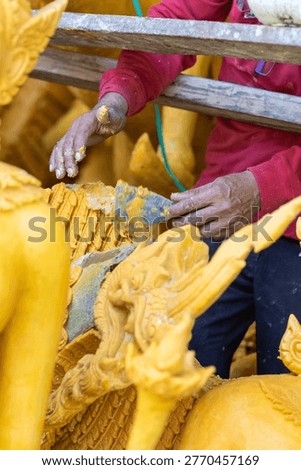 Close-up of an artisan's hands using a trowel to sculpt intricate details onto a large yellow wax figure for the traditional Candle Festival float.
